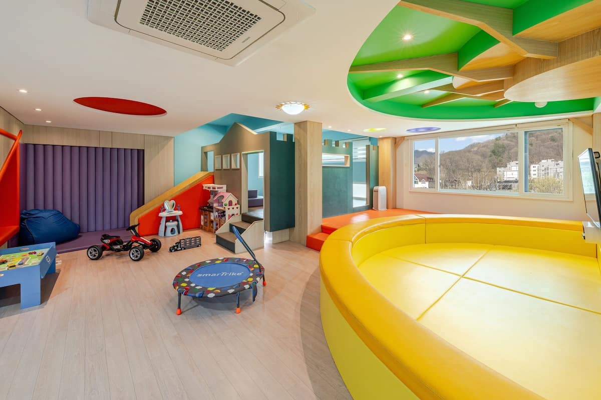 Zona de juegos infantiles con un tapete de juego amarillo grande, un pequeño trampolín y diversos juguetes.