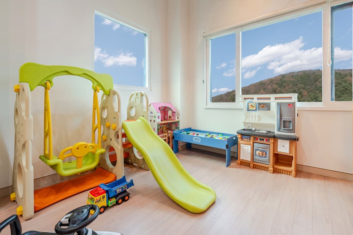 Una sala de juegos infantil con un tobogán, una cocina de juguete y vehículos de juguete.