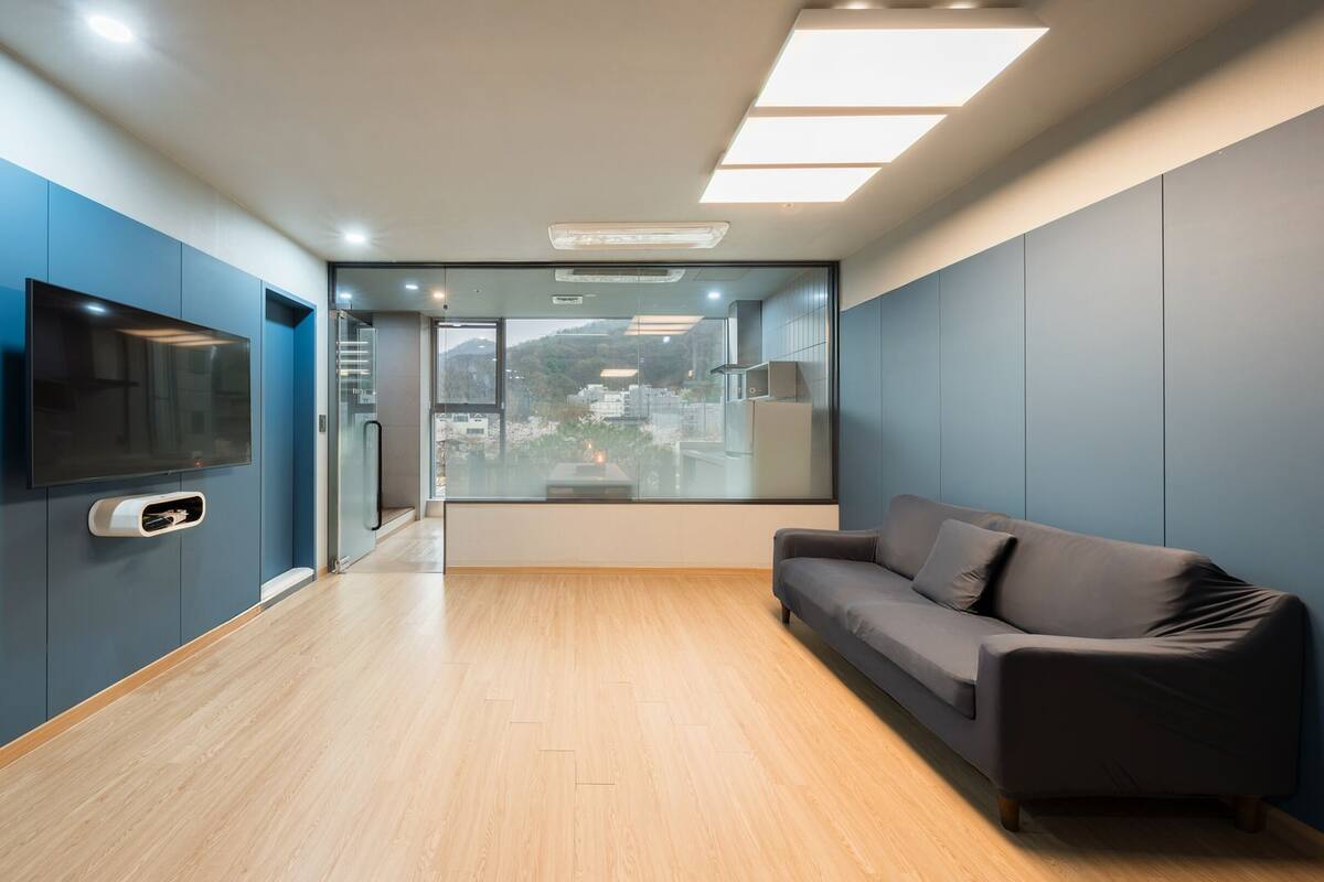 Un interior moderno con suelo de madera, un sofá gris y un televisor montado en la pared.
