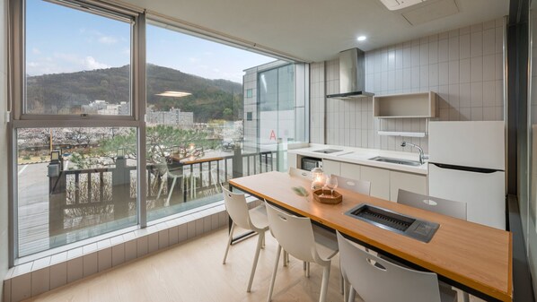A modern kitchen with a large window, white cabinetry, and a view of a cityscape and mountains. - Namyangju Aintio Pension (Namyangju)