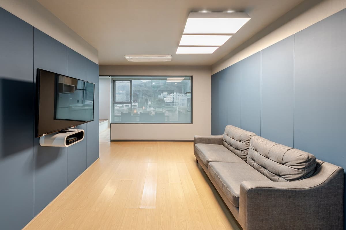 Una habitación moderna con una televisión de pantalla plana montada en la pared, un sofá gris y un ventanal con vistas a la ciudad.