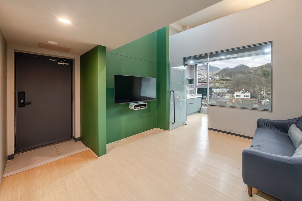 Un salón moderno con un sofá, un televisor de pantalla plana y un ventanal con vistas a un pueblo y montañas.