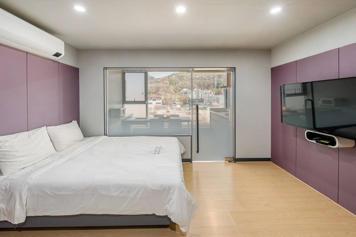 Un dormitorio con cama, televisor montado en la pared y puerta corrediza de vidrio a un balcón.