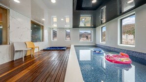 A spacious indoor swimming pool with wooden flooring, clear glass walls, and multiple windows offering views of the outdoors. - Namyangju Aintio Pension (Namyangju)