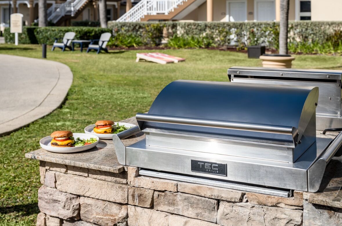 Un gril TEG avec des hamburgers servis sur des assiettes, le tout installé sur une plateforme en pierre à l’extérieur.