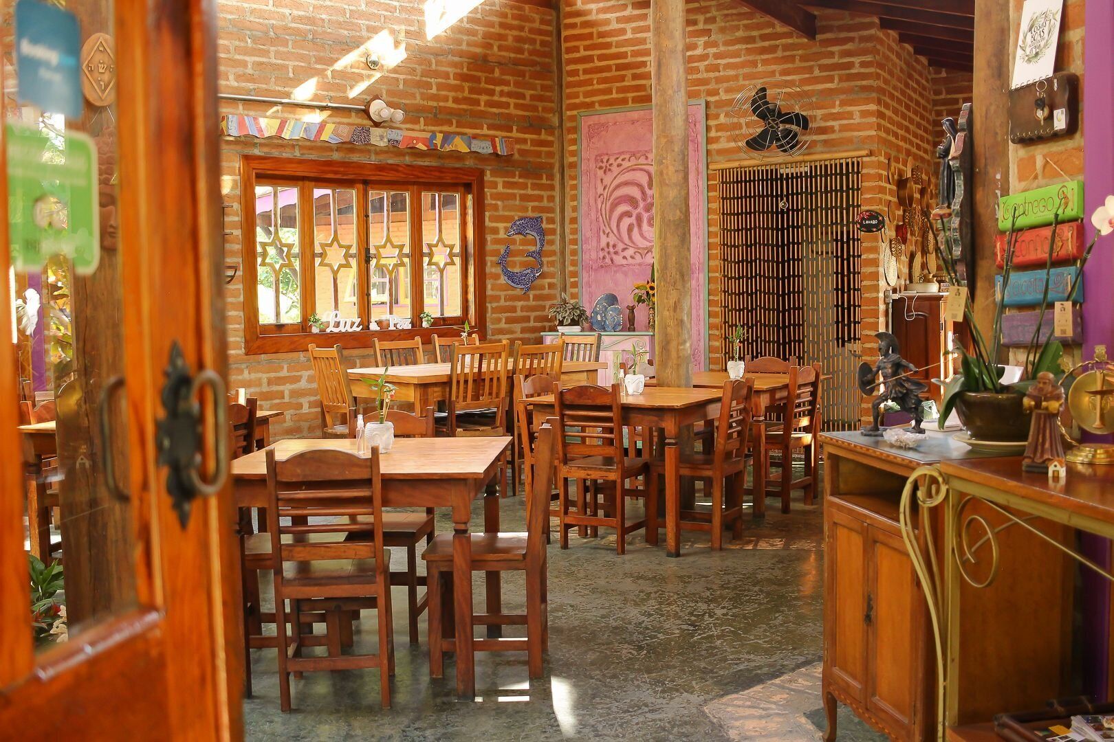 Uma zona de refeições rústica com mesas e cadeiras de madeira, parede de tijolo e vários objetos decorativos.