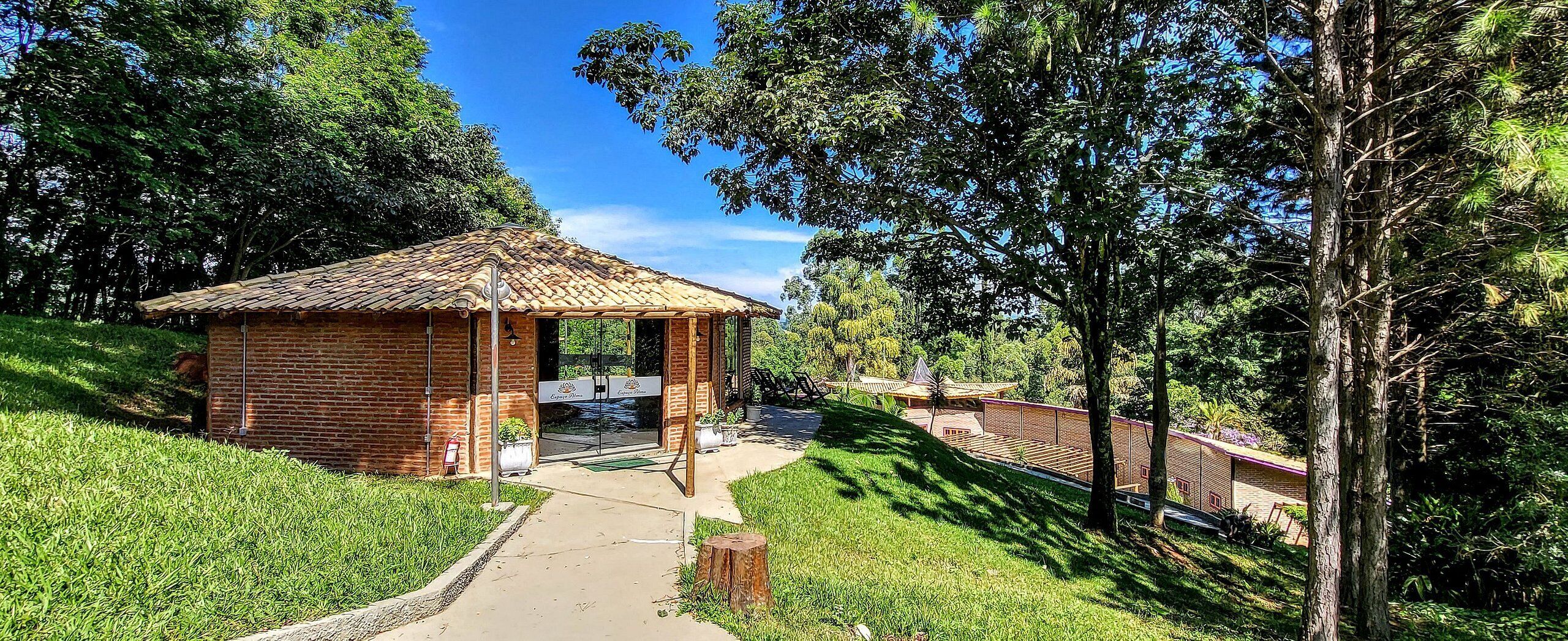 A small wooden pavilion with a tiled roof, surrounded by lush greenery and a clear sky.