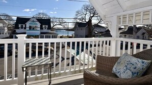A covered balcony with a white railing, wicker furniture, and a view of houses and a body of water.