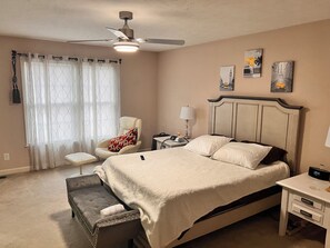 Cozy retreat with a large bed, bedside table, and chair, set against a neutral backdrop with framed artworks.