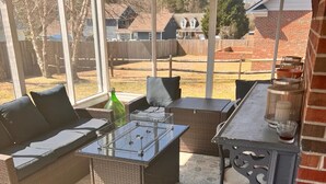 Une terrasse extérieure avec des meubles en osier, une table à plateau en verre et un mur en briques.