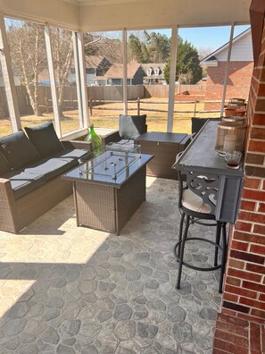 Relax in a serene outdoor space with a sofa, chair, and bar area, surrounded by a glass ceiling offering views of the neighborhood.