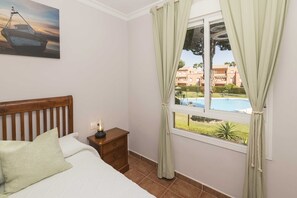 A bedroom with a bed, a nightstand, a lamp, and a window with curtains.