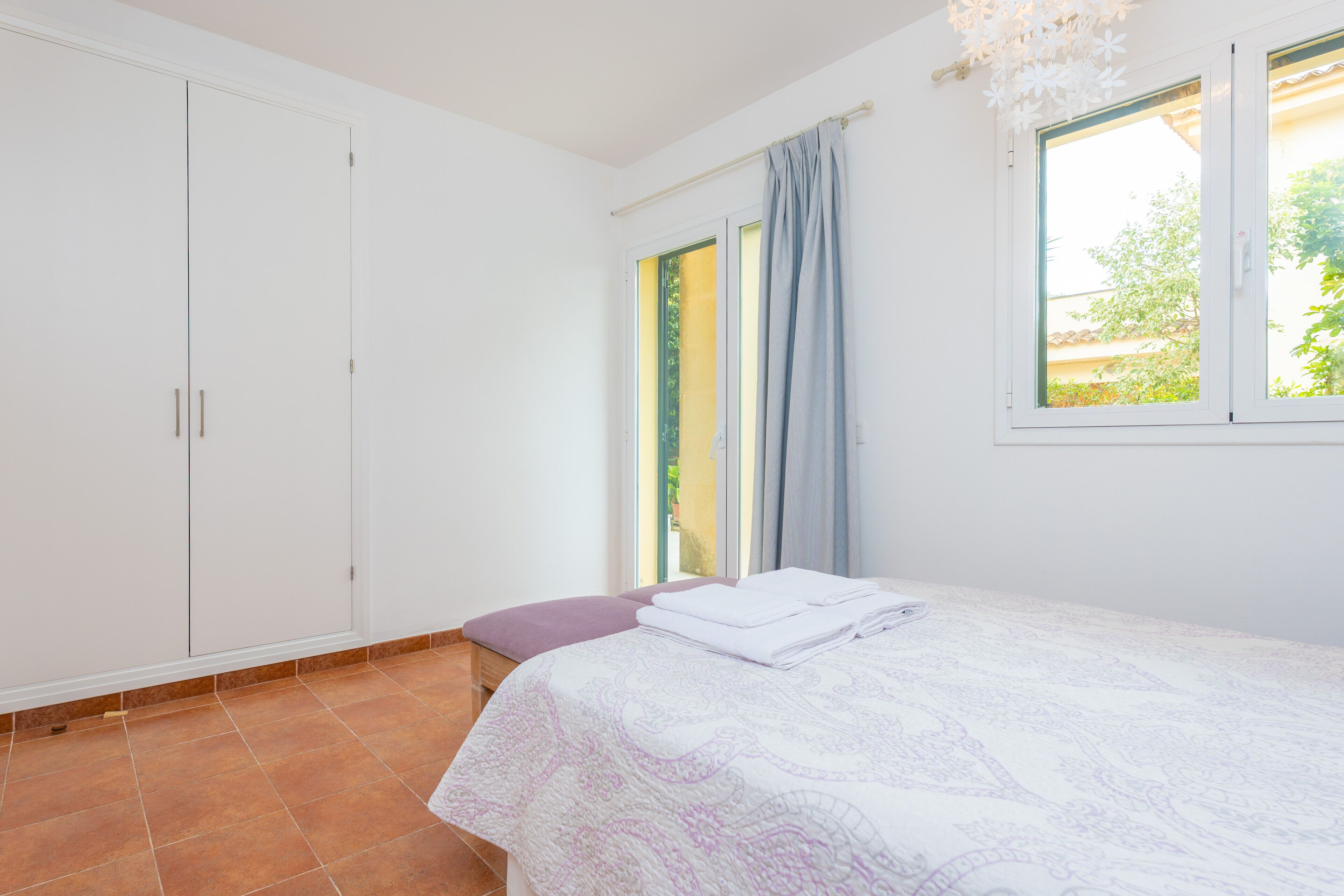 A bedroom with a bed, a window with curtains, a wardrobe, and a view of greenery outside.