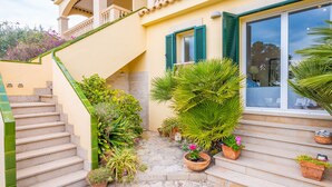 Una escalera conduce a un balcón con macetas y una ventana con persianas verdes.
