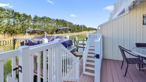A deck with a white railing, a table with chairs, and two boats docked by the water.