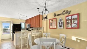 A kitchen with white chairs, a dining table, wooden cabinets, and a wall-mounted sign reading "Ocean City".