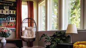 A room with a hanging chair, a lamp, a large plant, and a colorful rug.