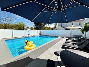 Relax by the pool surrounded by a white fence and lounge chairs.