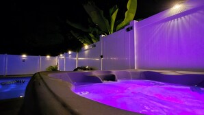 A hot tub area with a pool, surrounded by a white wall and illuminated by purple lights.