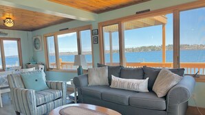 A cozy living room with a view of the water, featuring a sofa, armchair, and a wooden coffee table. - Oceanfront Escape: Deck & Granite Steps to Shore (Harpswell)