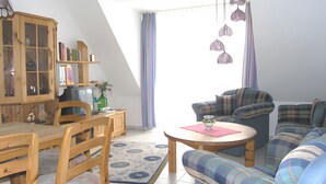 Una sala de estar acogedora con una mesa de comedor de madera, sillas, un sofá y un televisor.