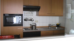 Una cocina con armarios de madera, microondas, hervidor, pileta y utensilios colgantes.