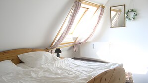 Un dormitorio con cama de madera, ventana con cortinas, espejo y radiador.