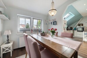 A dining area with a wooden table, chairs, a chandelier, and a view of the outside. - Apartment 'Schlafmütze' with Shared Terrace, Shared Garden and Wi-Fi (Cuxhaven)