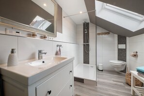 A modern bathroom with a skylight, a large mirror, a sink, a toilet, and a shower area. - Apartment 'Schlafmütze' with Shared Terrace, Shared Garden and Wi-Fi (Cuxhaven)