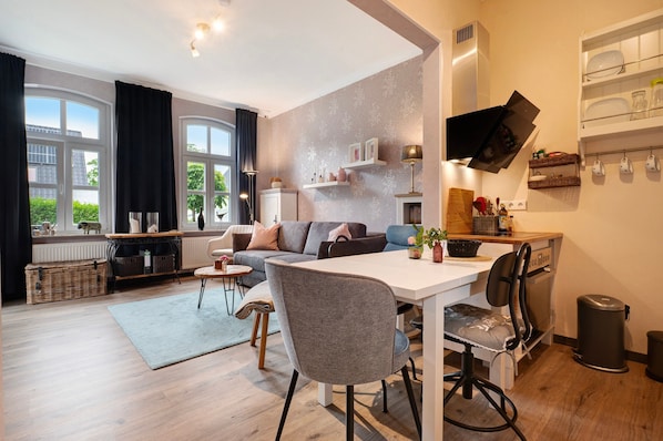 Een moderne woonkamer met een eethoek, grote ramen en een keuken met een hangende televisie.