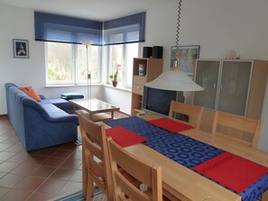 Una sala moderna con un sofá azul, una mesa de comedor de madera y un televisor.