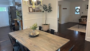 Un coin repas avec une table en bois, des chaises, un lustre, des plantes en pot et une vue sur le salon.