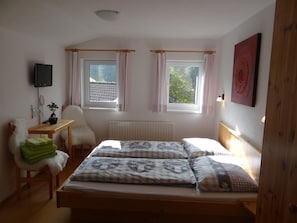 Une chambre à coucher comprenant un lit, un bureau, une chaise, un radiateur et deux fenêtres avec des rideaux.