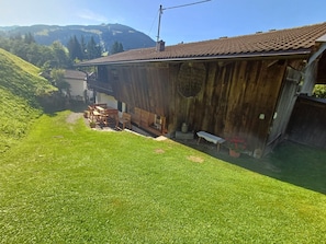 Un bâtiment rustique en bois, doté d’un toit en tuiles, d’un petit espace extérieur aménagé avec des bancs et d’une cour gazonnée.