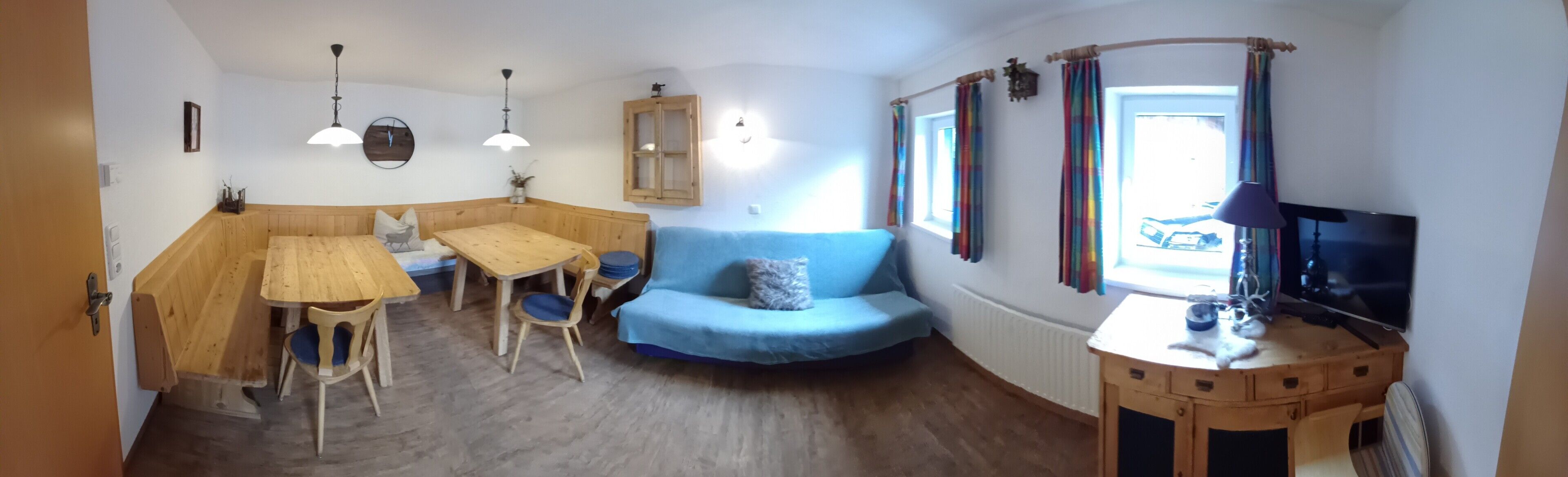 Et hyggeligt rum med et træspisebord, en blå sofa og et fjernsyn på et træstel.