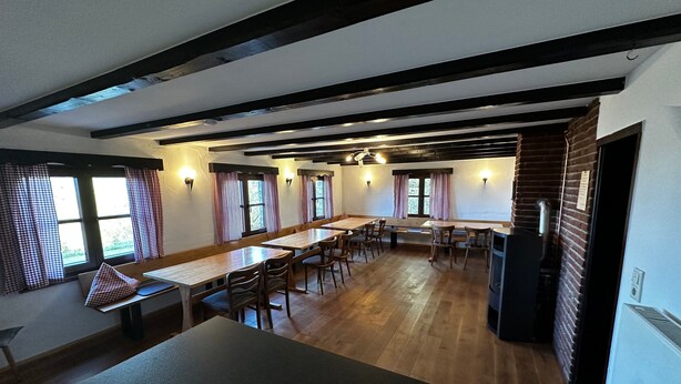 A dining area with wooden tables and chairs, a brick wall, and windows with checkered curtains. - Ski Lodge of the Skiclub Brilon with Mountain Views and Shared Terrace (Brilon)