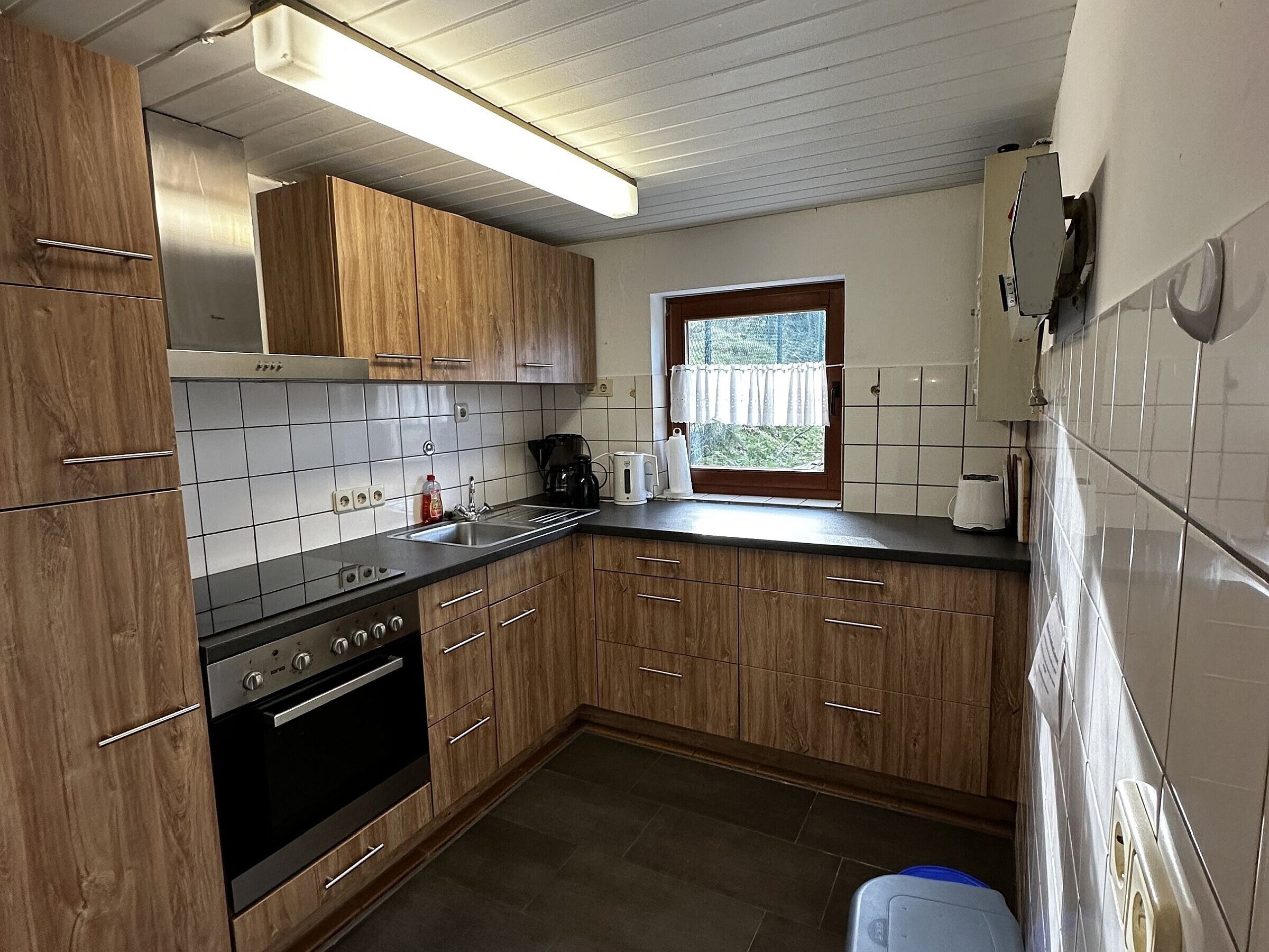 A kitchen with wooden cabinets, a stainless steel sink, a stove, and a window with a view.