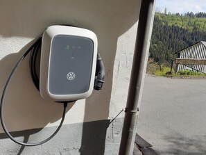 A charging station with a Volkswagen logo, attached to a wall with a metal pole nearby.