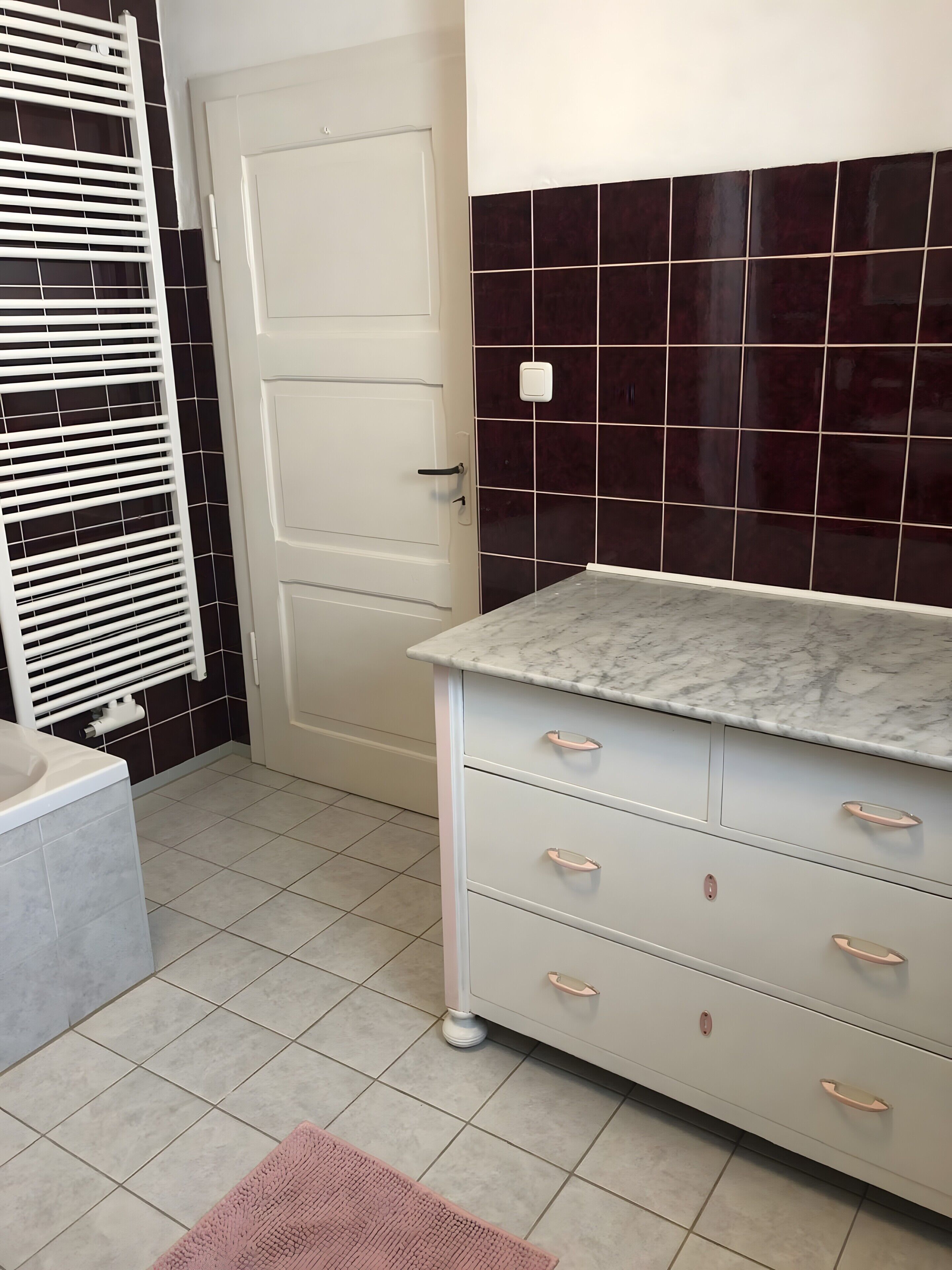 A bathroom with a white door, a marble countertop, and a tiled floor.