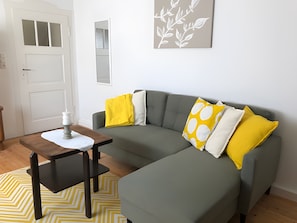 A living room with a grey sofa, a small table with a candle, and a yellow patterned rug. - "My Holiday Home Rosenbusch 1" with Private Terrace, Garden and Wi-Fi (Kemmern)