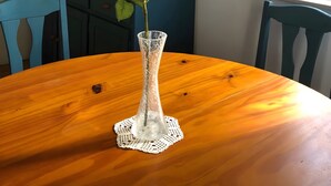 Ein Holztisch mit einer klaren Glasvase, in der eine Rose steht.