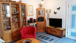 A compact living space with a wooden cabinet, a red chair, a television, and a kitchen area. - Holiday Apartment 'Sternenhof' with Wi-Fi (Breisach am Rhein)