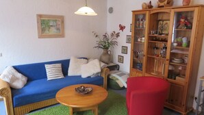 A living room with a blue sofa, a red armchair, a wooden cabinet, and a green rug. - Holiday Apartment 'Sternenhof' with Wi-Fi (Breisach am Rhein)