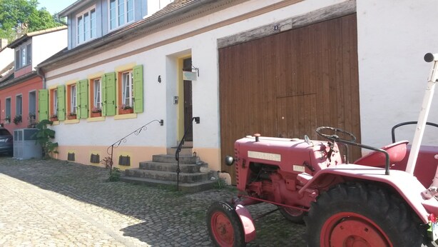 A red tractor parked in front of a building with a large wooden door, a staircase, and a cobblestone path. - Holiday Apartment 'Sternenhof' with Wi-Fi (Breisach am Rhein)