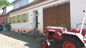 Un tractor rojo estacionado frente a un edificio con una puerta de madera grande, una escalera y un camino adoquinado.
