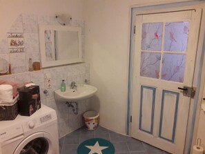 Un baño pequeño con lavadora, un lavabo, un espejo y una puerta con ventana.