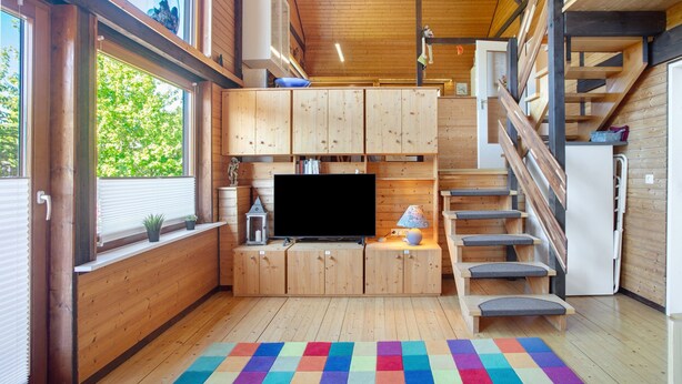A compact kitchen with wooden cabinets, a TV, and a staircase.