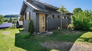 A modern house with a sloped roof, a wooden door, and solar panels in the yard.
