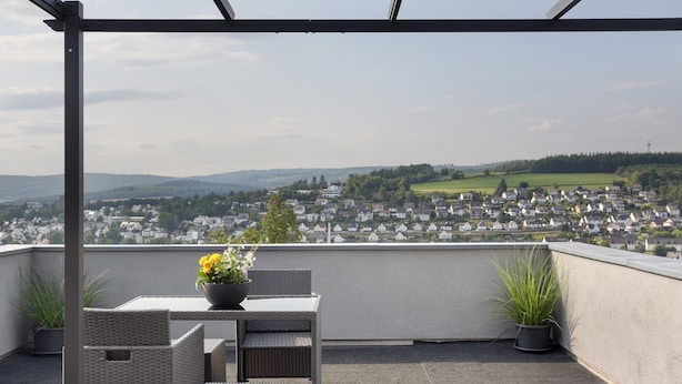 A balcony with wicker furniture, potted plants, and a view of a town and hills. - Holiday Apartment 'Zum Hasen' with Mountain View, Private Terrace and Wi-Fi (Meschede)