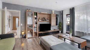 A modern living room with a flat-screen TV, a bookshelf, a sofa, a coffee table, and a dining table. - Holiday Apartment 'Zum Hasen' with Mountain View, Private Terrace and Wi-Fi (Meschede)